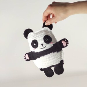 May include: A handmade crochet panda bear toy. The panda has a white body with a black stripe, black ears, and black arms and legs. The panda has a smiling face with pink cheeks and is being held up.