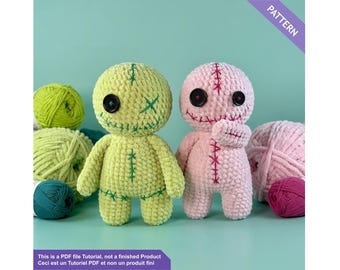 May include: Two handmade crochet dolls, one light green and one pink, with stitched details and button eyes. The dolls are displayed with balls of yarn in shades of green, pink, and teal. The image includes text that reads "PATTERN".