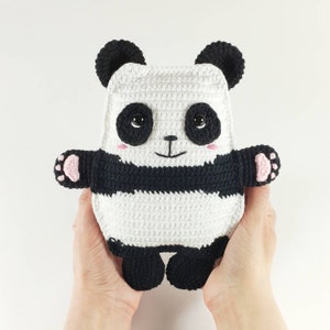 May include: A handmade crochet panda bear with black and white stripes, black eyes, and pink accents on the paws and cheeks. The panda has small black ears and is held up against a white background.