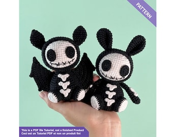 May include: Two crocheted Halloween-themed toys: a bat and a bunny. Both are black with white skeleton detailing and facial features. The bat has wings, and the bunny has long ears. The toys are held in a hand. The image includes the text "PATTERN".