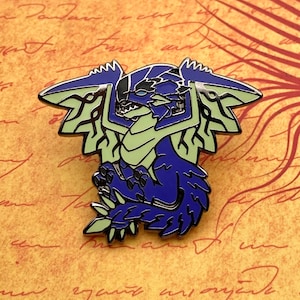 Op de afbeelding: Een paarse en groene emaille pin van een draak met vleugels en een kroon. De draak is opgerold in een verdedigende positie.