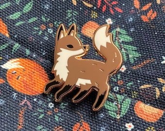 May include: A gold-colored enamel pin featuring a cartoon fox with a white chest and tail. The fox is standing on all fours and has a friendly expression.