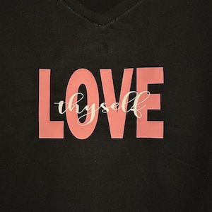 May include: Black v-neck t-shirt with the words "LOVE thyself" printed in pink and white.
