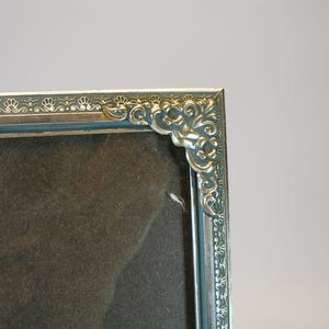 May include: A silver picture frame with an ornate design around the edge. The frame is empty and ready for a photo.