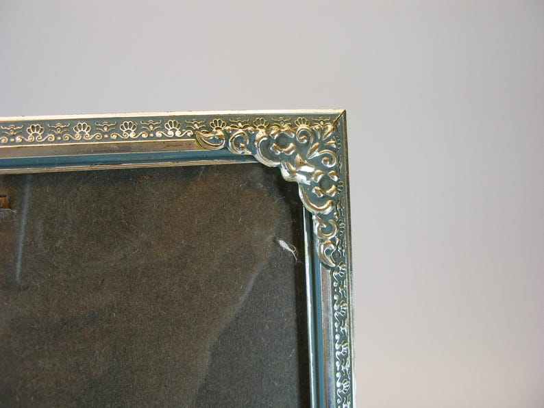 May include: A silver picture frame with an ornate design around the edge. The frame is empty and ready for a photo.
