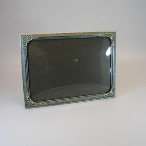 May include: A silver picture frame with an ornate design. The frame has a glass front and a dark brown mat.
