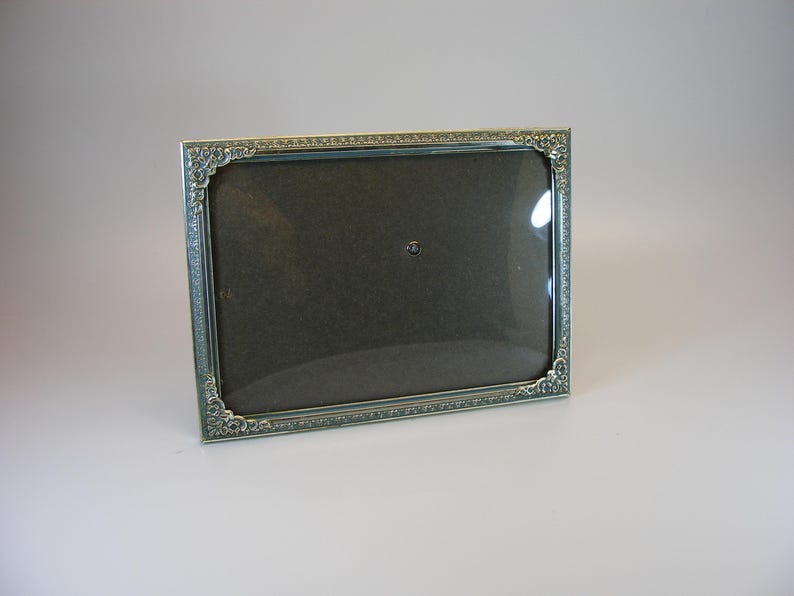 May include: A silver picture frame with an ornate design. The frame has a glass front and a dark brown mat.