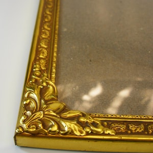 Può includere: Una cornice dorata con un design ornamentale. La cornice ha un bordo decorativo e un angolo dettagliato.