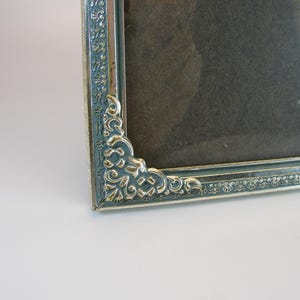 May include: A silver picture frame with an ornate design. The frame has a dark gray mat and a clear glass front.