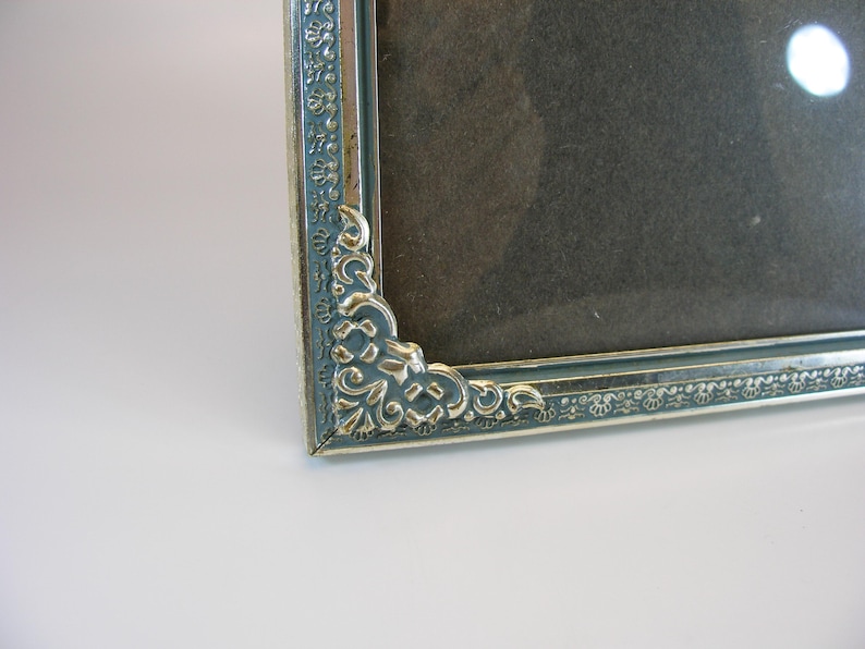 May include: A silver picture frame with an ornate design. The frame has a dark gray mat and a clear glass front.