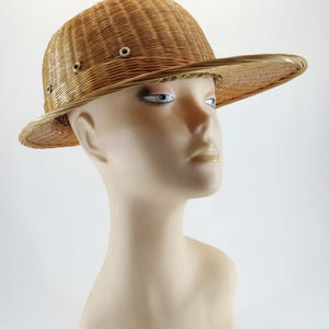 May include: A woven straw hat with a wide brim and a slightly domed crown. The hat features a series of small, evenly spaced eyelets around the crown. The hat is a light tan color and appears to be made of natural fibers.