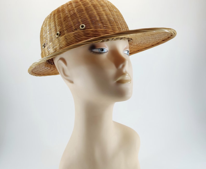 May include: A woven straw hat with a wide brim and a slightly domed crown. The hat features a series of small, evenly spaced eyelets around the crown. The hat is a light tan color and appears to be made of natural fibers.