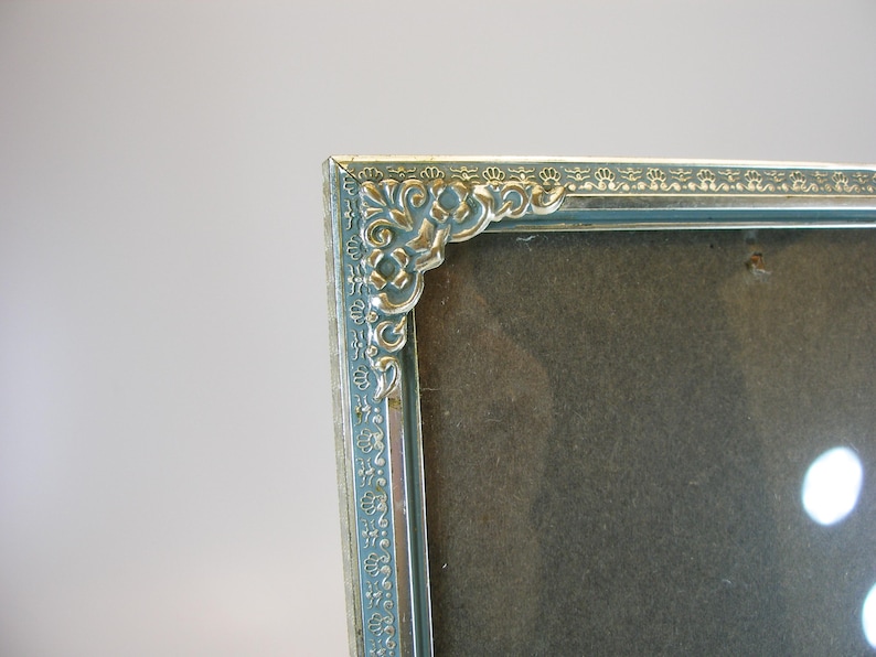 May include: A silver picture frame with an ornate design around the edge. The frame is empty and has a light blue background.