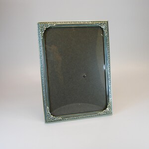 May include: A silver picture frame with an ornate design. The frame has a glass front and a black backing.