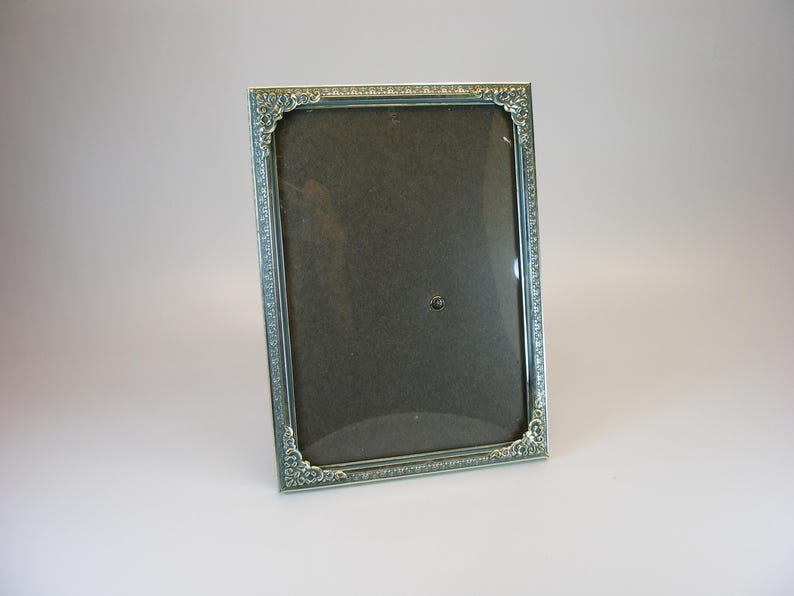 May include: A silver picture frame with an ornate design. The frame has a glass front and a black backing.