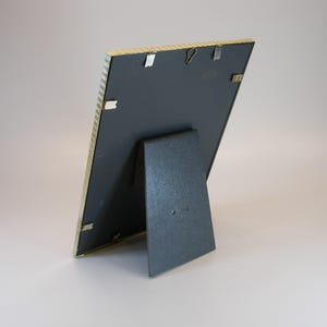 May include: A gold-colored picture frame with a black mat and a stand on the back. The frame is made of a textured material.