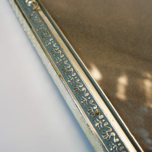 May include: Close-up of a silver picture frame with a blue and silver decorative border. The frame is made of metal and has a glass front.