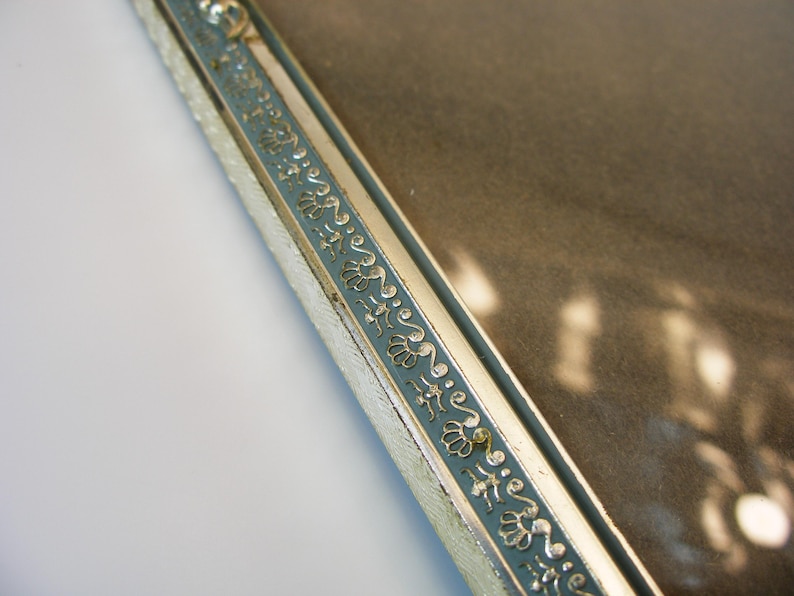 May include: Close-up of a silver picture frame with a blue and silver decorative border. The frame is made of metal and has a glass front.