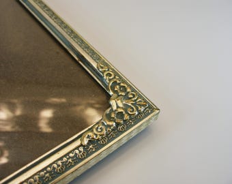 May include: A gold picture frame with an ornate design. The frame has a silver finish and a decorative border.