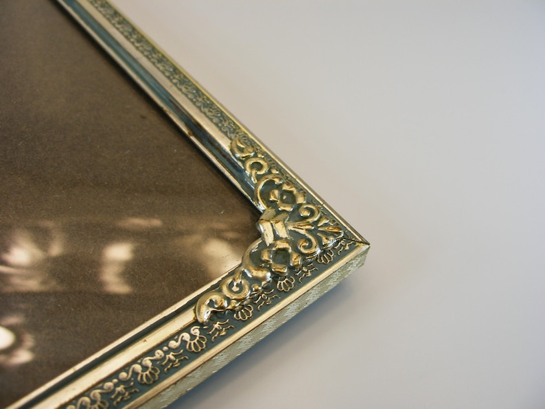 May include: A gold picture frame with an ornate design. The frame has a silver finish and a decorative border.