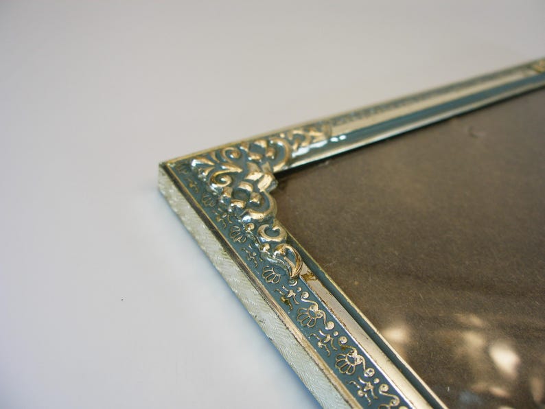 May include: A silver picture frame with a blue and gold ornate design. The frame is empty and ready for a photo.