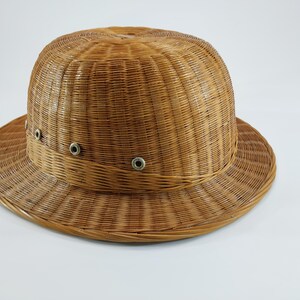 May include: A woven brown hat with a rounded crown and a wide brim. The hat features a band around the crown with three metal eyelets. The hat is made of a natural fiber and has a textured appearance. The hat is suitable for sun protection.