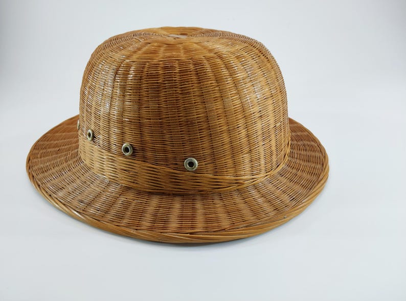 May include: A woven brown hat with a rounded crown and a wide brim. The hat features a band around the crown with three metal eyelets. The hat is made of a natural fiber and has a textured appearance. The hat is suitable for sun protection.