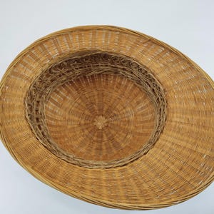 May include: A woven straw hat with a wide brim and a circular crown. The hat is made of natural-colored straw and has a detailed woven pattern. The hat's design is suitable for sun protection.