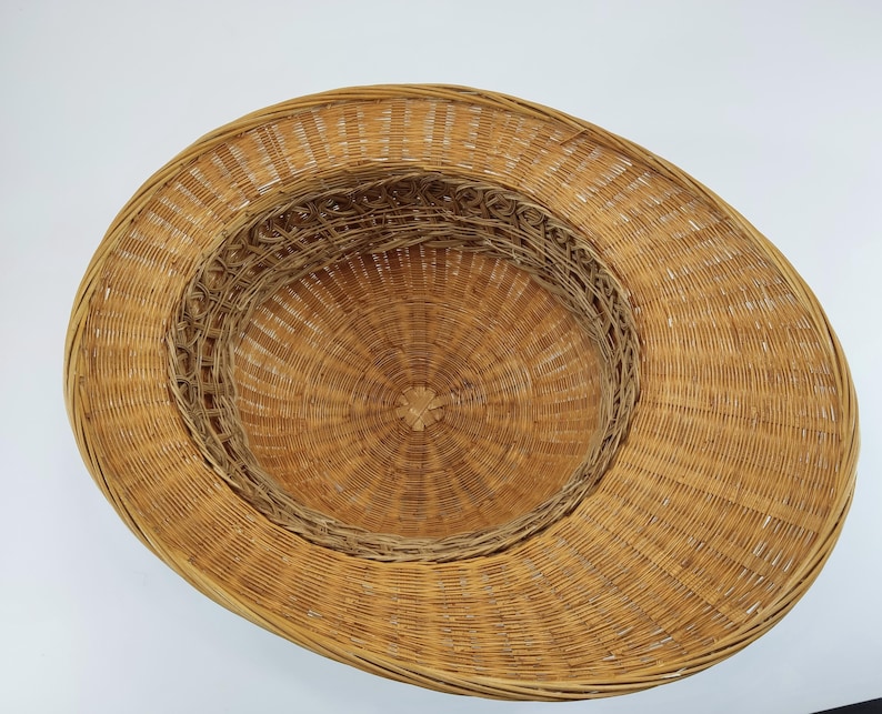 May include: A woven straw hat with a wide brim and a circular crown. The hat is made of natural-colored straw and has a detailed woven pattern. The hat's design is suitable for sun protection.