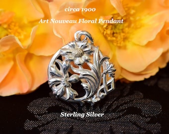 Può includere: Un pendente floreale Art Nouveau in argento sterling, circa 1900. Il pendente presenta un design floreale dettagliato con un fiore centrale e foglie circostanti. Il pendente è posto su uno sfondo di fiori arancioni.