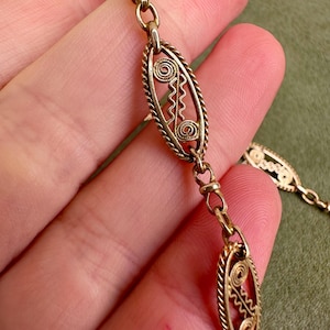May include: A gold chain necklace with oval-shaped links featuring intricate filigree designs. The links are connected by smaller, round links.