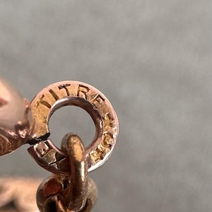 May include: Close-up of a gold chain with a clasp that reads "TITRE 18K" in a circular design.