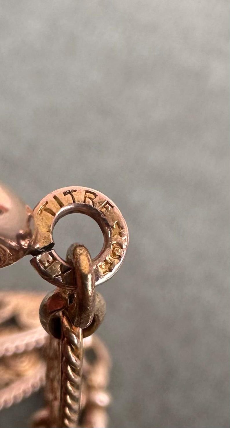 May include: Close-up of a gold chain with a clasp that reads "TITRE 18K" in a circular design.