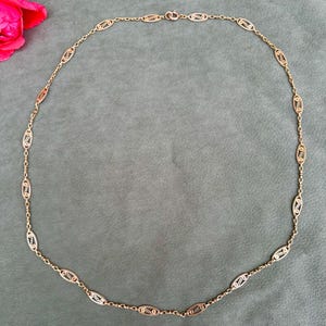 May include: A gold chain necklace with oval-shaped links. The links are intricately designed with a delicate pattern.