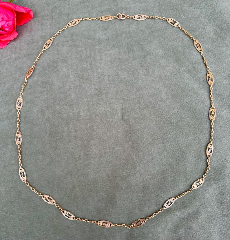 May include: A gold chain necklace with oval-shaped links. The links are intricately designed with a delicate pattern.