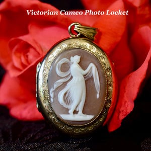 May include: Oval gold-tone Victorian cameo photo locket with a white carved figure on a brown background. The locket is surrounded by a decorative border and is set against a backdrop of red and yellow roses. The text "Victorian Cameo Photo Locket" is visible.