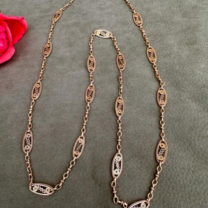 May include: A gold chain necklace with oval-shaped links. Each link is intricately designed with a filigree pattern.