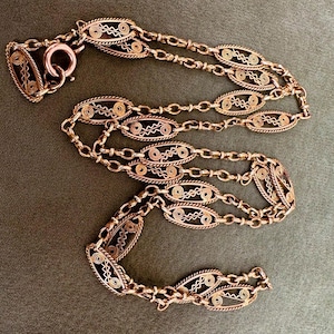 May include: A long, delicate copper chain necklace with intricate oval-shaped links. The chain is made of multiple strands of wire woven together to create a delicate, openwork design.