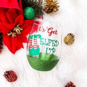 May include: A clear glass wine glass with a green glitter bottom and a red and green "Let's Get Elfed Up" design.