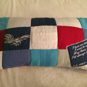 May include: A patchwork pillow made from blue, white, and red fabric. The pillow has an embroidered eagle on one side and a message that reads "These are shirts I used to wear Hug them tight I'll always be there. Love Dad 9.5.1998-1.14.2016" on the other side.