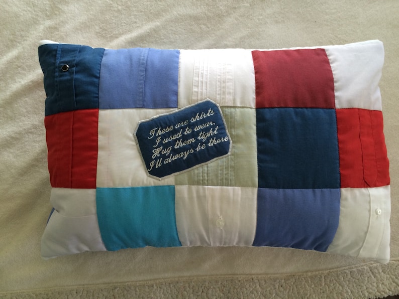 May include: A patchwork pillow with a blue, red, and white color scheme. The pillow has a small embroidered tag that reads "These are shirts I used to wear. Hug them tight I'll always be there."