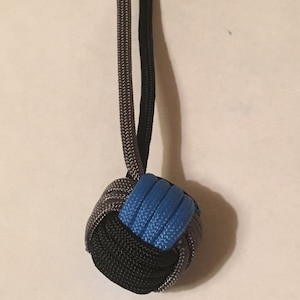 May include: A blue, black, and gray paracord knot tied into a ball shape. The knot is hanging from two cords.