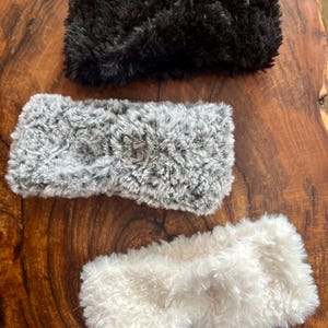 K&ouml;nnte beinhalten: Drei flauschige Stirnb&auml;nder mit einem gedrehten Knoten in der Mitte. Das Set besteht aus einem einfarbigen schwarzen Stirnband, einem grau-wei&szlig; melierten Stirnband und einem cremefarbenen Stirnband aus weichem, pl&uuml;schigem Material.