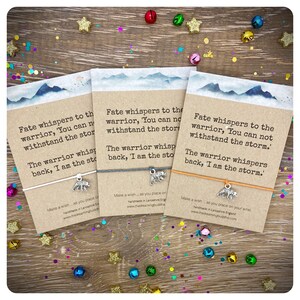 May include: Three colorful bracelets with inspirational quotes and a silver bear charm. The quotes are "Fate whispers to the warrior, 'You can not withstand the storm.' The warrior whispers back, 'I am the storm.'"