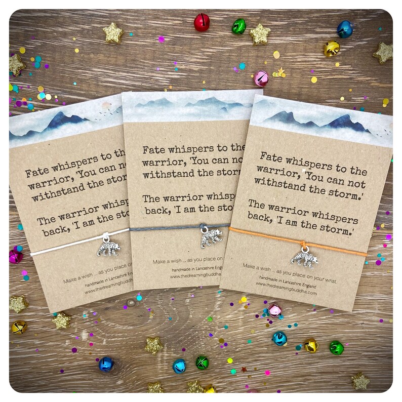 May include: Three colorful bracelets with inspirational quotes and a silver bear charm. The quotes are "Fate whispers to the warrior, 'You can not withstand the storm.' The warrior whispers back, 'I am the storm.'"