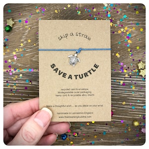 Pode incluir: Um bracelete de corda de cânhamo azul com um amuleto de tartaruga de prata. O cartão diz "skip a straw save a turtle" e inclui informações sobre os materiais reciclados usados para fazer o bracelete.