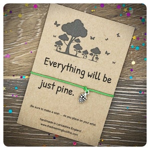 Könnte beinhalten: Ein grünes Armband aus Schnur mit einem silbernen Tannenzapfen-Anhänger. Die an das Armband befestigte Karte lautet "Everything will be just pine." und "Be sure to make a wish... as you place on your wrist. Handmade in Lancashire England www.thedreamingbuddha.com"