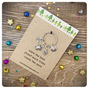 May include: A brown card with the text "save the bees plant more trees clean the seas" and the website address "www.thedreamingbuddha.com". A silver key chain with a turtle, a bee, a pine cone, and a round charm is attached to the card.