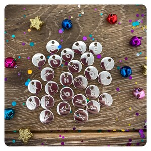 May include: A collection of silver metal letter charms with a variety of letters of the alphabet. The charms are arranged on a wooden surface with colorful confetti.