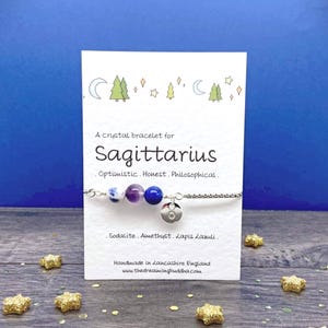 May include: A crystal bracelet for Sagittarius, featuring sodalite, amethyst, and lapis lazuli beads. The bracelet is on a card with text that reads "Optimistic. Honest. Philosophical." and "Handmade in Lancashire England."